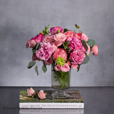 A Case of Hot Fever arrangement featuring fresh garden roses and ranunculus in a tall clear vase, designed in a circular formation, perfect for all occasions.