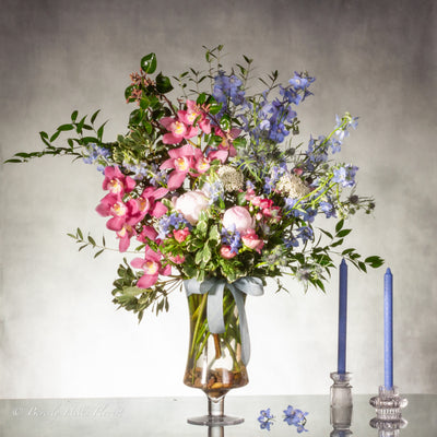 A Floral Tale of Love and Beauty with pink cymbidium orchids and delphiniums in a tall glass vase, available for same-day delivery by Beverly Hills Florist.