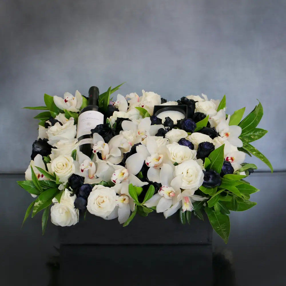A Gift For You arrangement with black and white roses, cymbidium orchids, greens in a black wooden box with wine and a candle, by Beverly Hills Florist.