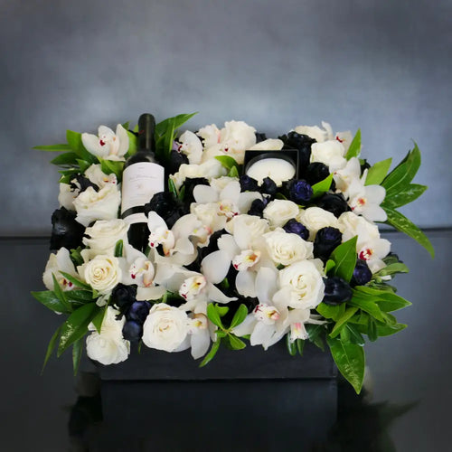 A Gift For You arrangement with black and white roses, cymbidium orchids, greens in a black wooden box with wine and a candle, by Beverly Hills Florist.