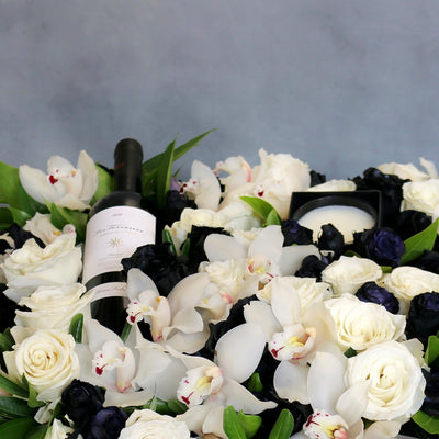 A Gift For You arrangement with black and white roses, cymbidium orchids, greens in a black wooden box with wine and a candle, by Beverly Hills Florist.