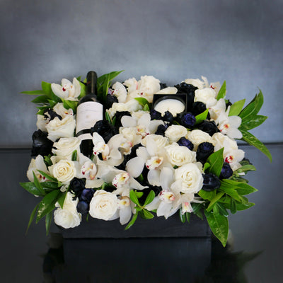 A Gift For You arrangement with black and white roses, cymbidium orchids, greens in a black wooden box with wine and a candle, by Beverly Hills Florist.