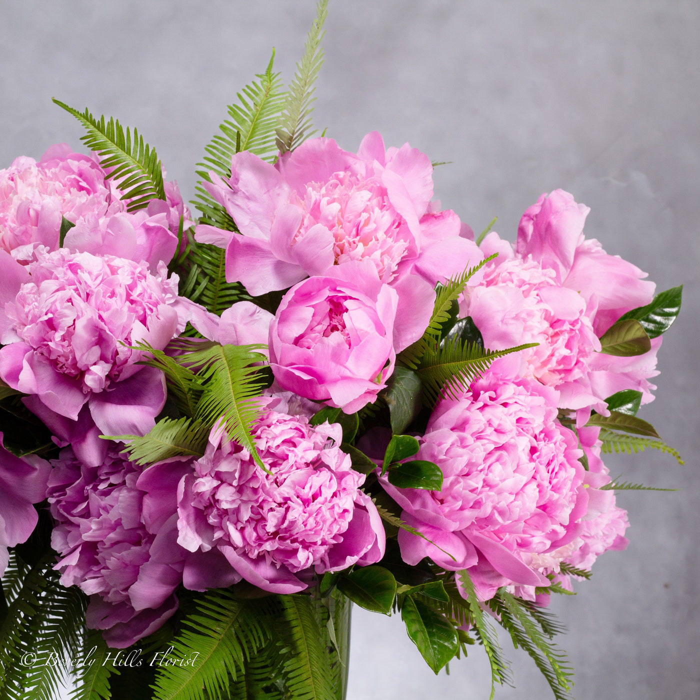 Elegant pink peony arrangement in a clear 12-inch glass vase with umbrella ferns and Gardenia foliage.