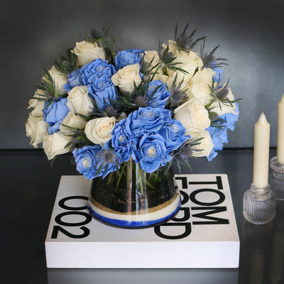 Blue Me Away arrangement with blue and white roses, thistles, and colored sand in a modern vase, available for same-day delivery by Beverly Hills Florist.