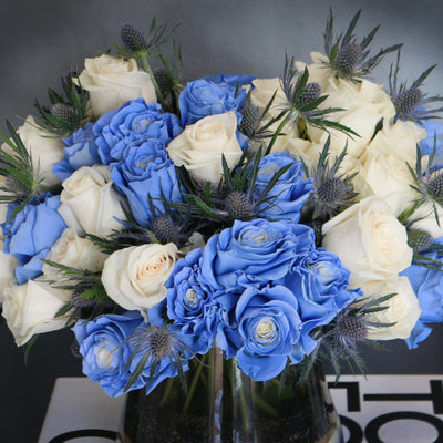 Blue Me Away arrangement with blue and white roses, thistles, and colored sand in a modern vase, available for same-day delivery by Beverly Hills Florist.