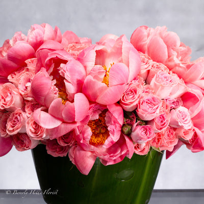 Luxurious arrangement of coral peonies and pink spray roses in a pedestal vase, available for same-day delivery.