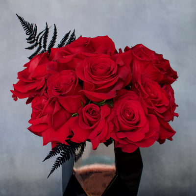 Deep red roses in a black geometric glass vase, measuring 14x9 inches, modern and elegant floral arrangement.