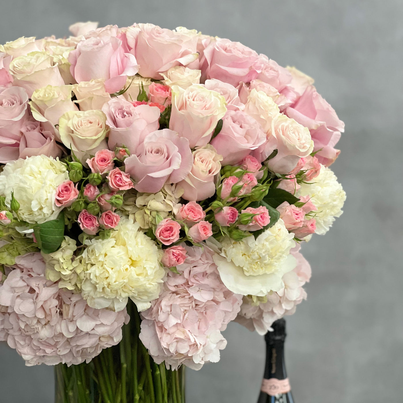 Elegant arrangement of over 100 pale pink roses and peonies in a sleek glass vase, 28 inches tall, designed by Beverly Hills Florist.