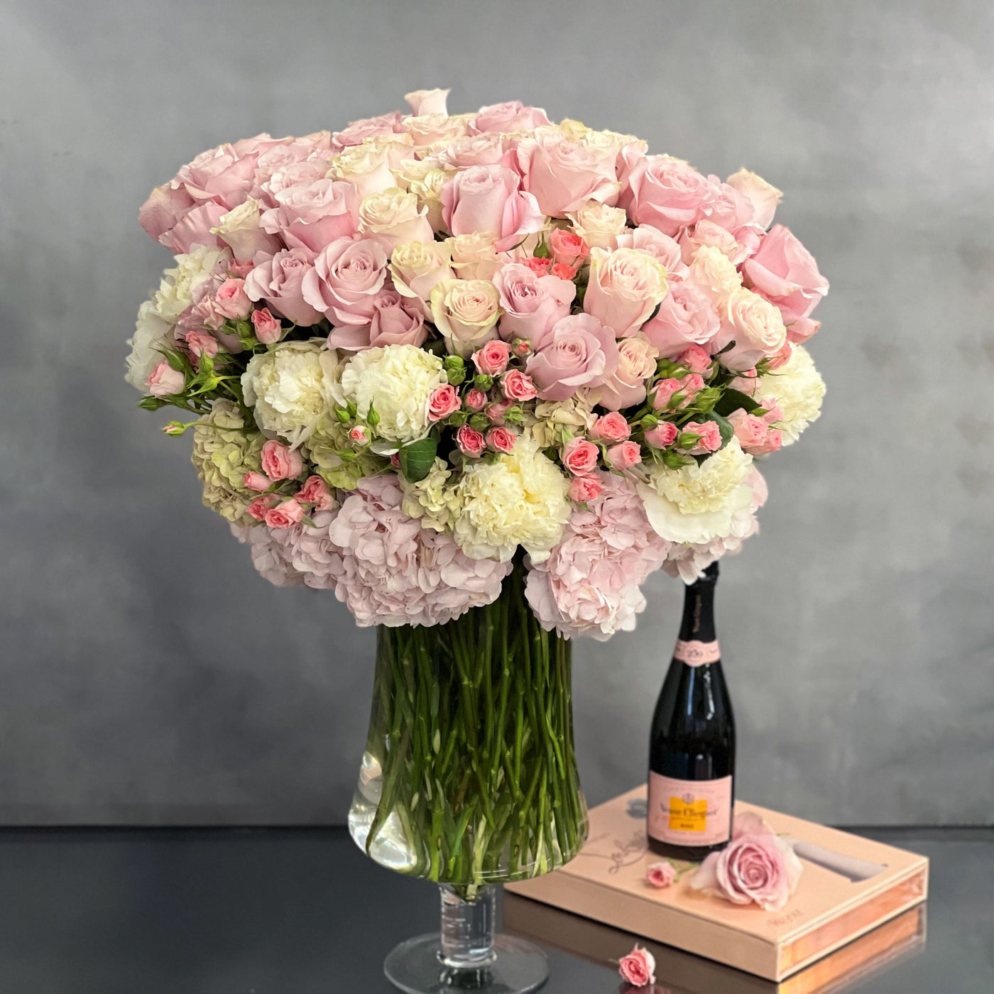 Elegant arrangement of over 100 pale pink roses and peonies in a sleek glass vase, 28 inches tall, designed by Beverly Hills Florist.