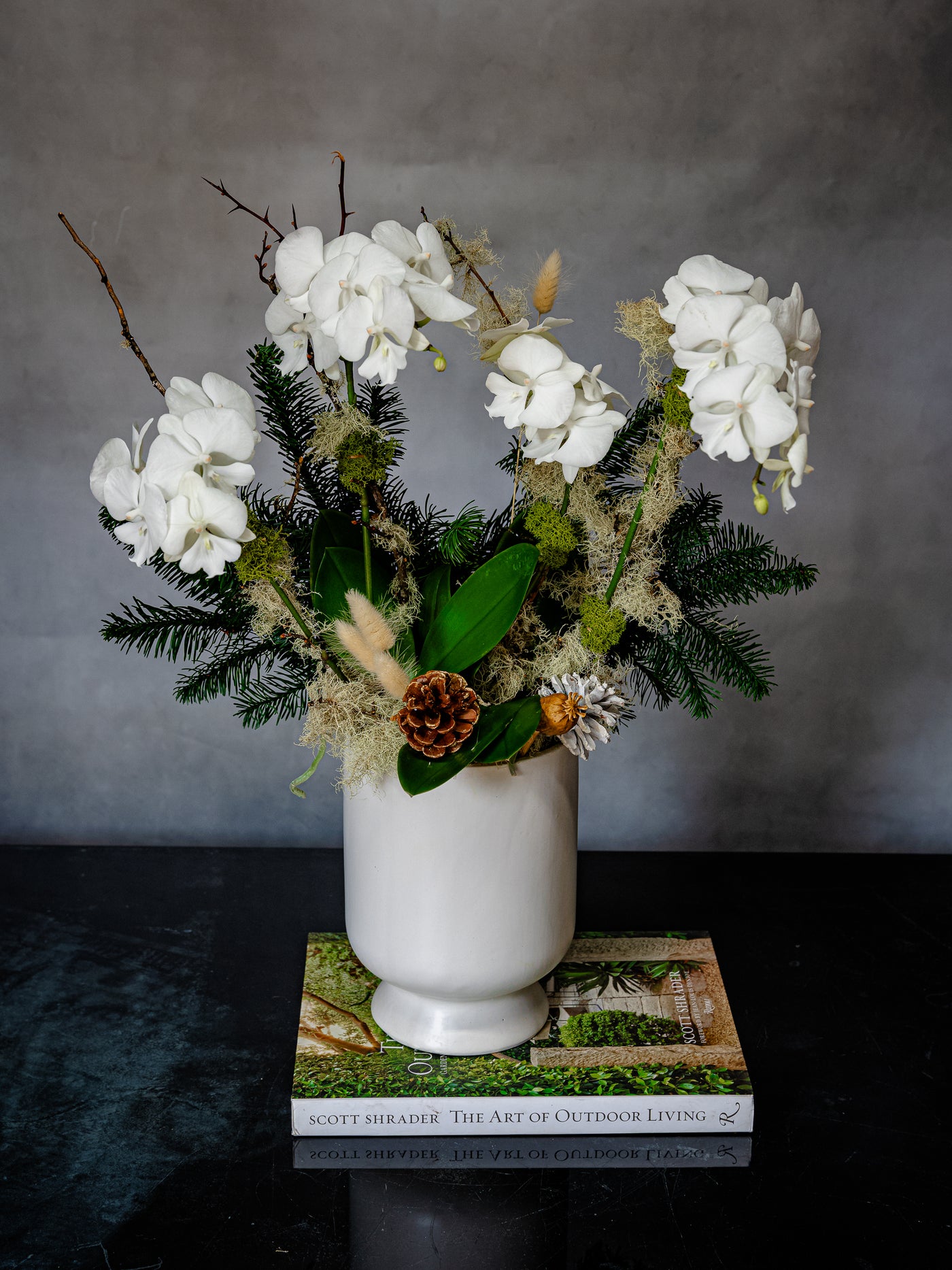 Elegant white orchid holiday arrangement in a round white ceramic vase with festive holiday accents.