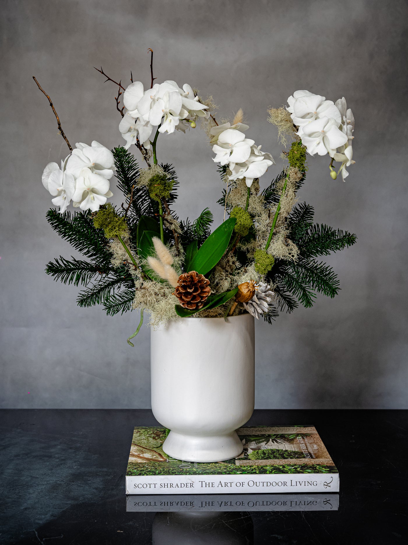 Elegant white orchid holiday arrangement in a round white ceramic vase with festive holiday accents.