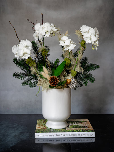 Elegant white orchid holiday arrangement in a round white ceramic vase with festive holiday accents.