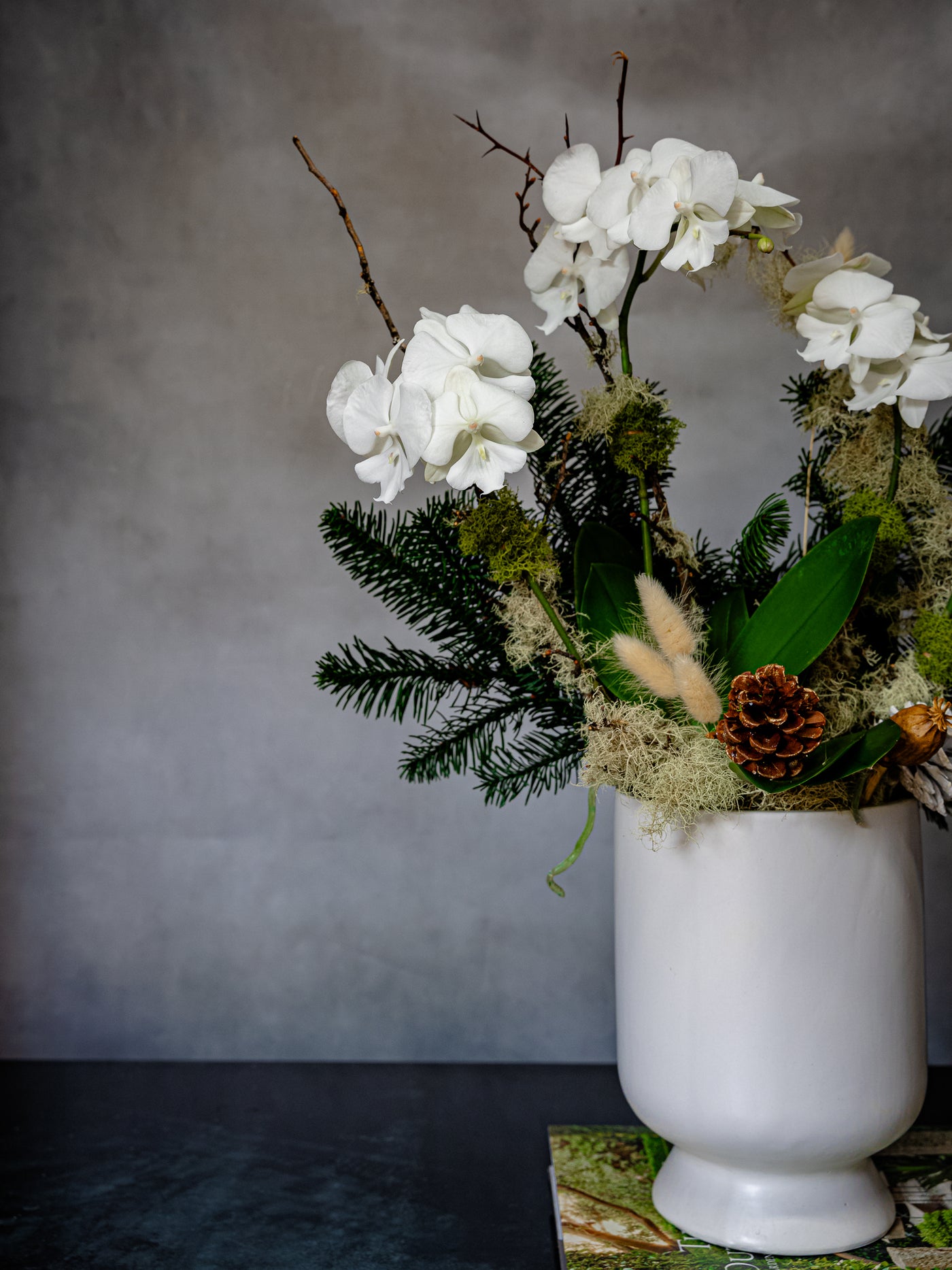 Elegant white orchid holiday arrangement in a round white ceramic vase with festive holiday accents.