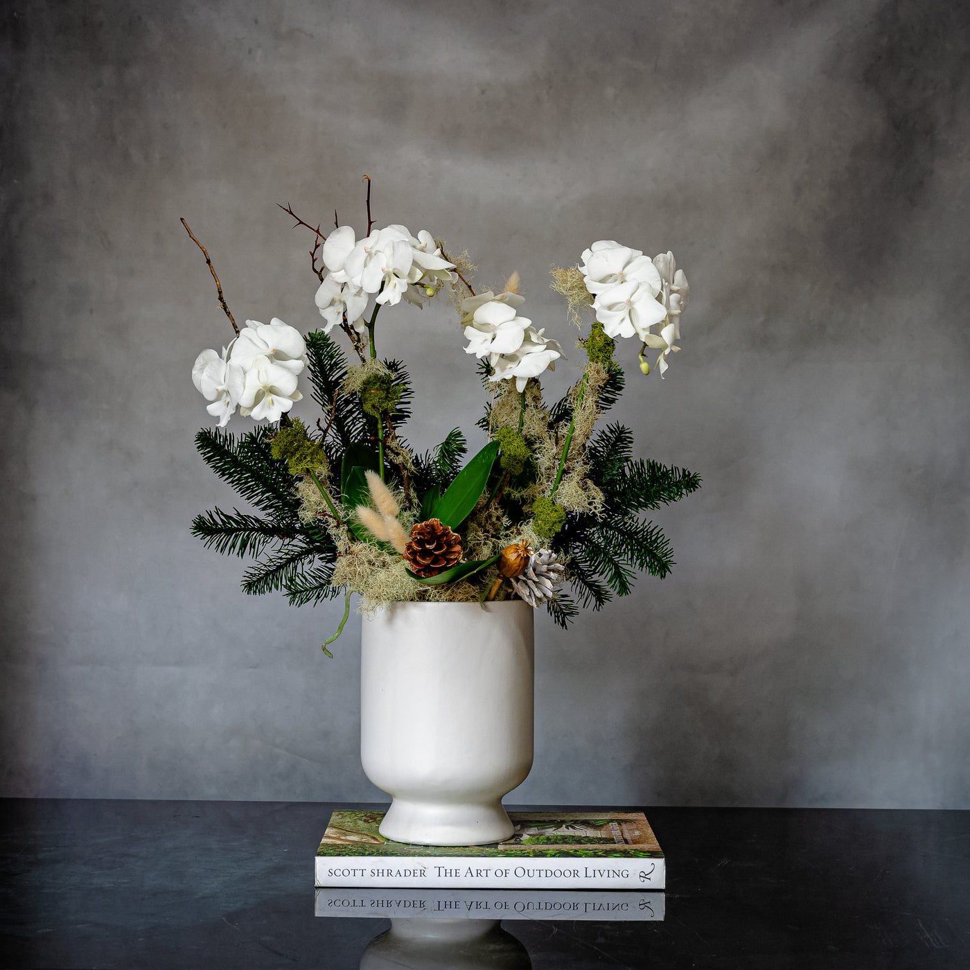 Elegant white orchid holiday arrangement in a round white ceramic vase with festive holiday accents.