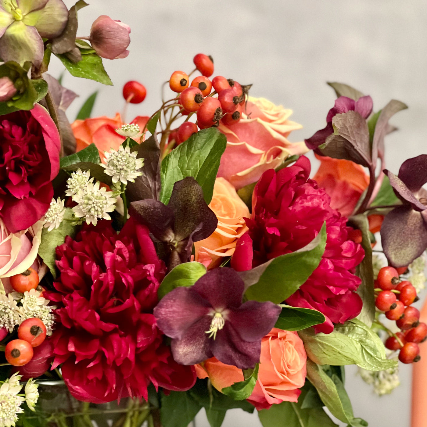 Majestic winter arrangement with orange roses, burgundy peonies, and winter accents in a glass vase – available for same-day delivery by Beverly Hills Florist.