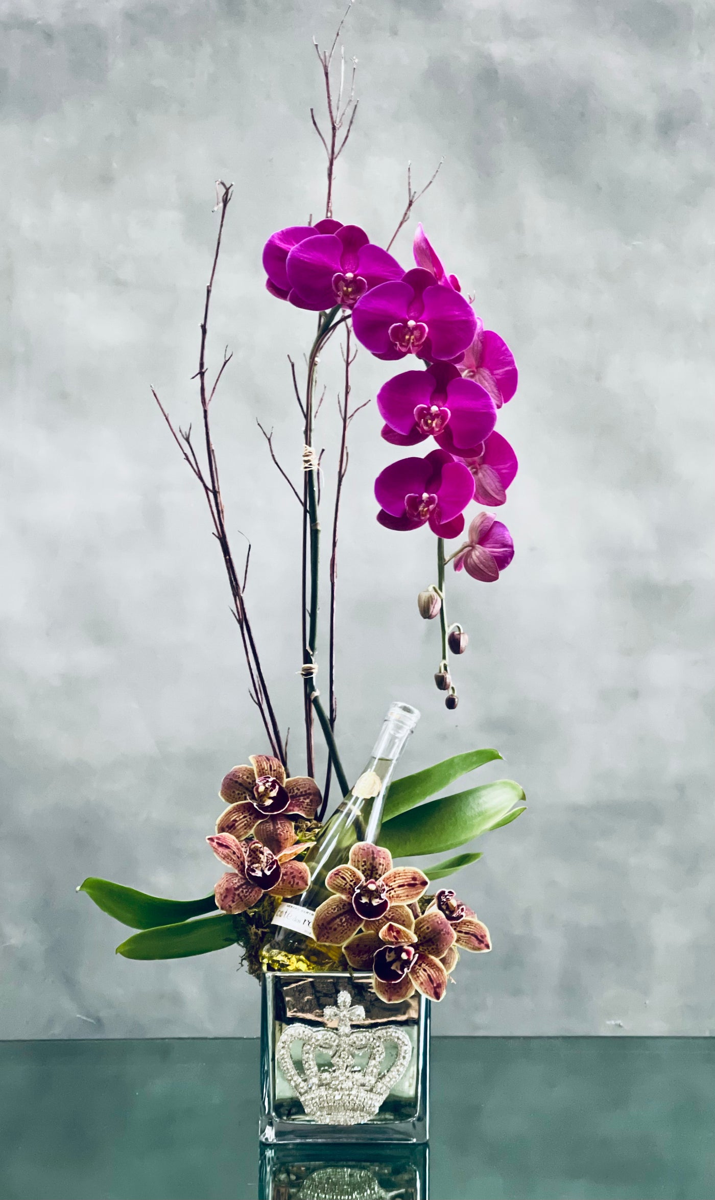 Beverly Hills Florist presents this duo orchid arrangement for same day delivery ! Our team has created can be made and sent out on the same day ! Beverly Hills Florist placed Amethyst cascading orchid with Cymbidium orchids and a half bottle Cotes de Roses Chardonnay are nested in a crown jeweled vase. A wonderful Love and Romance gesture. 