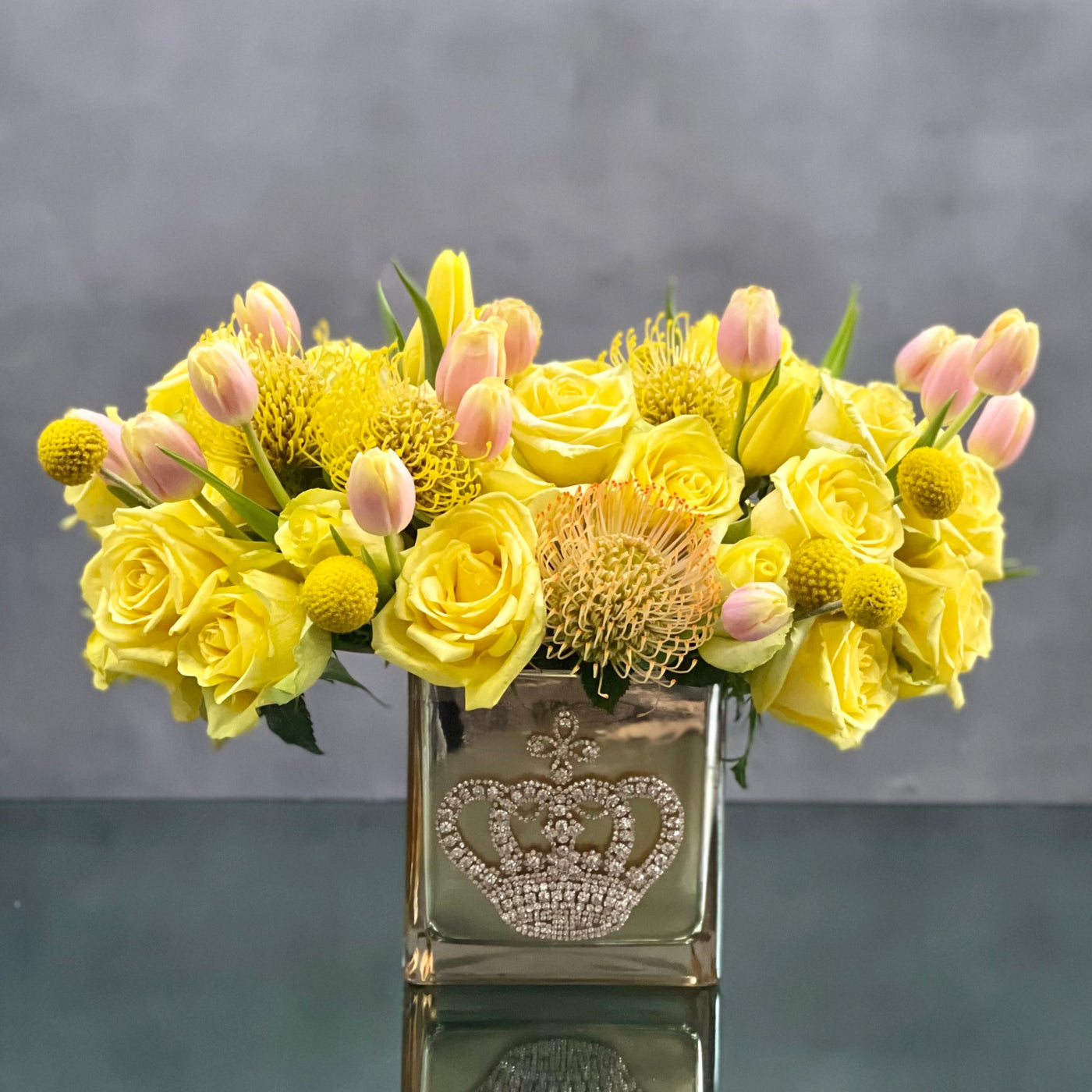 Beverly Hills Florist offers Queen Bee for same day delivery! This striking arrangement of yellow roses, tulips and protea in a gold crown jeweled glass vase. Fit for a queen! Wonderful for a Thank you, Friends day or a pick me up !