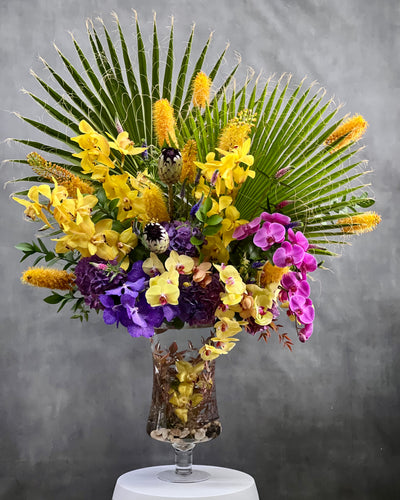 A Spectacular Floral Fantasy featuring extravagant and exotic blooms in tropical colors on a grand scale by Beverly Hills Florist for occasions like congrats, new baby, just because, love and romance. Vibrant seasonal blooms paint the oranges, deep pinks, purples, lime greens and yellow orchids and other floral. Large tropical leaves lined vase with this amazing design and colors. It's a one-of-a-kind, dynamic presentation that will be the center of attention wherever it is placed. Approx: 16 W x 30" H.