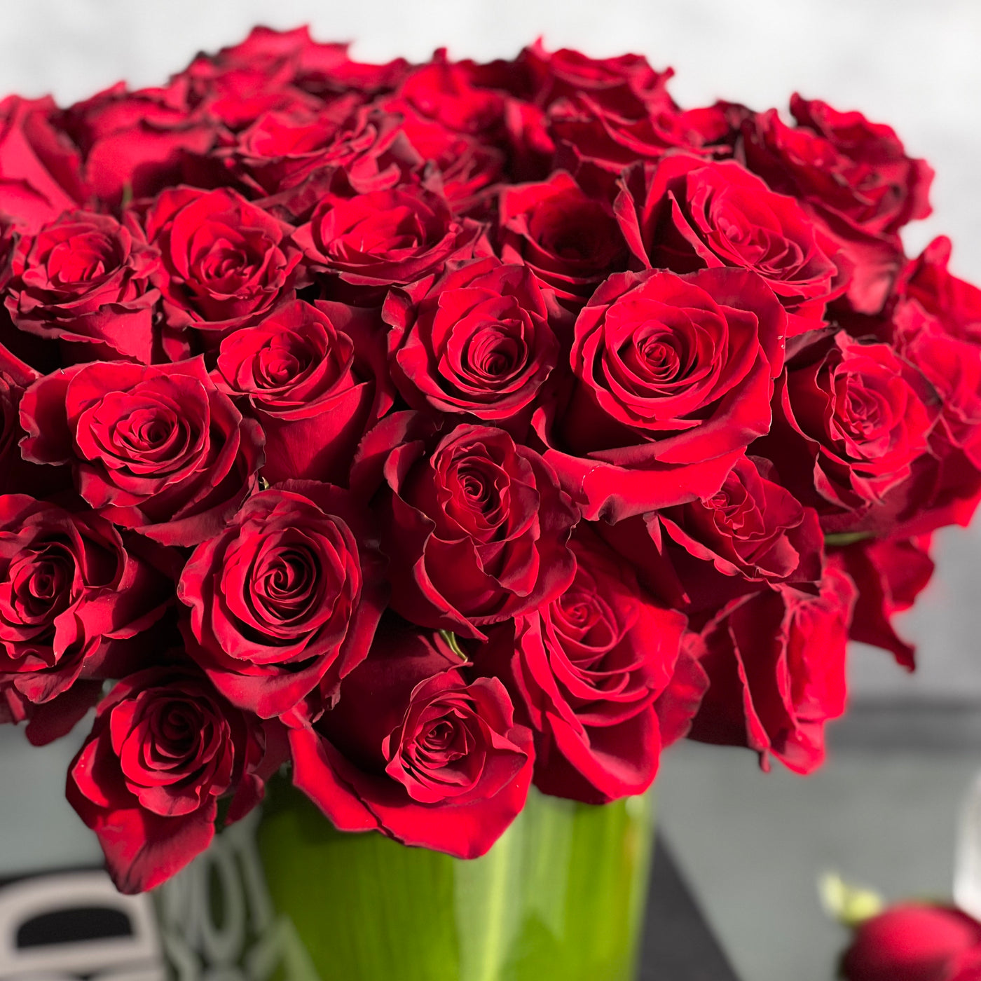 Kiss from a Rose arrangement with up to 75 fresh roses in a minimalist 7-inch glass vase lined with leaves, measuring 14 inches tall and 15 inches wide.