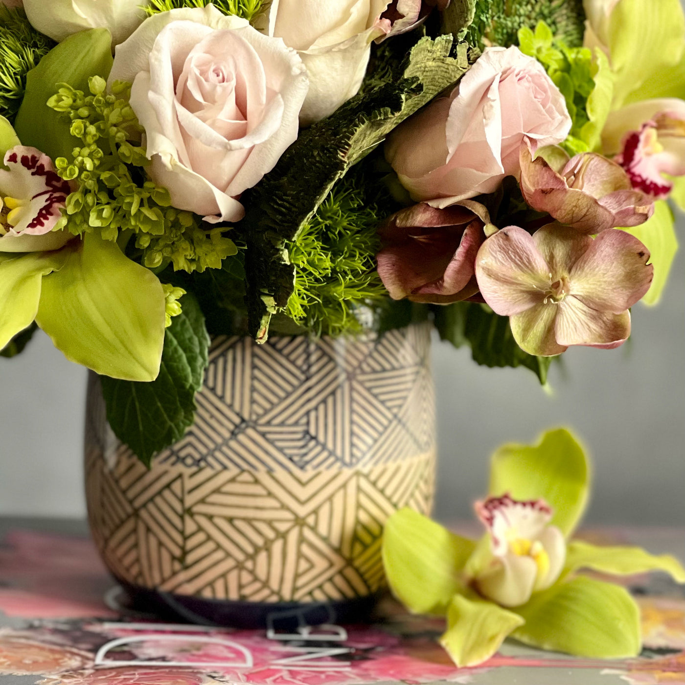 A Rustic Romance arrangement with cream roses, green cymbidium orchids, and seasonal greens in a geometric earth-toned vase, same-day delivery by Beverly Hills Florist.