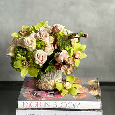 A Rustic Romance arrangement with cream roses, green cymbidium orchids, and seasonal greens in a geometric earth-toned vase, same-day delivery by Beverly Hills Florist.