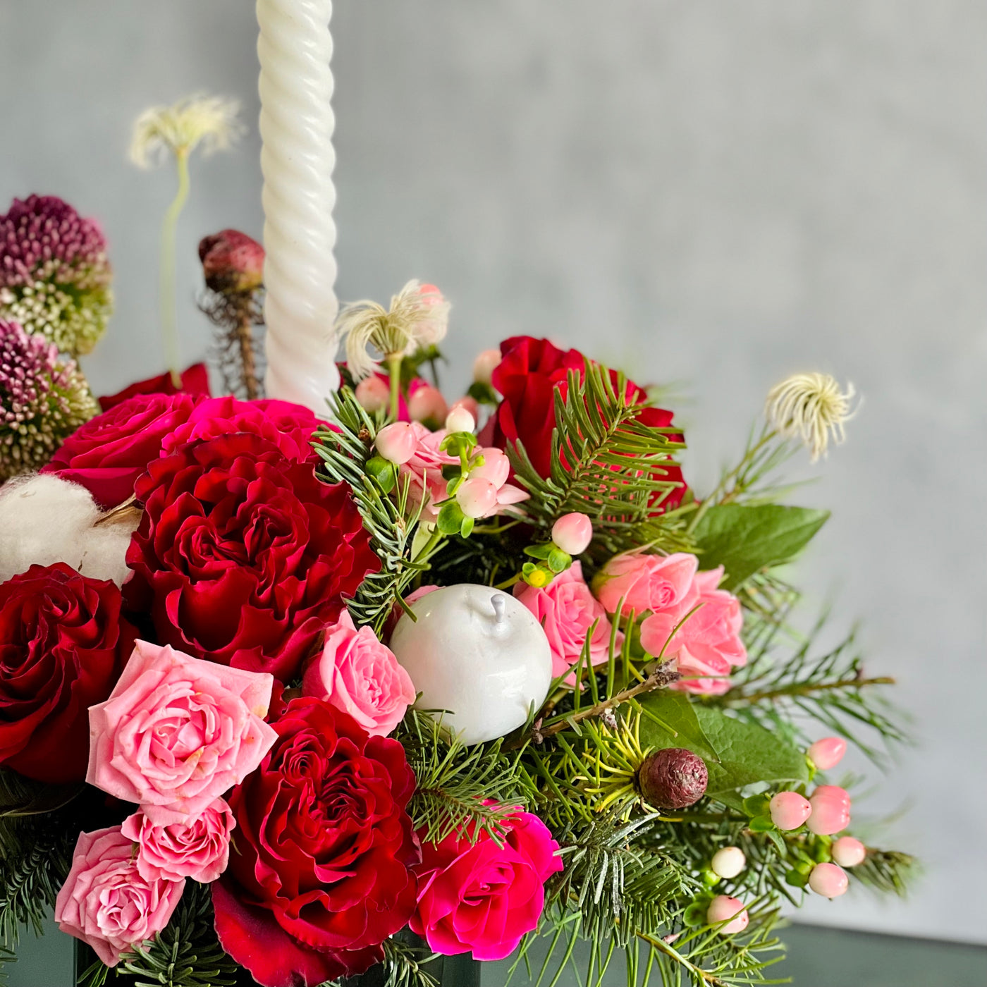 Festive Christmas centerpiece with red and pink roses, seasonal greens, berries, and glowing tapers, approx. 14 inches tall, for same-day delivery.