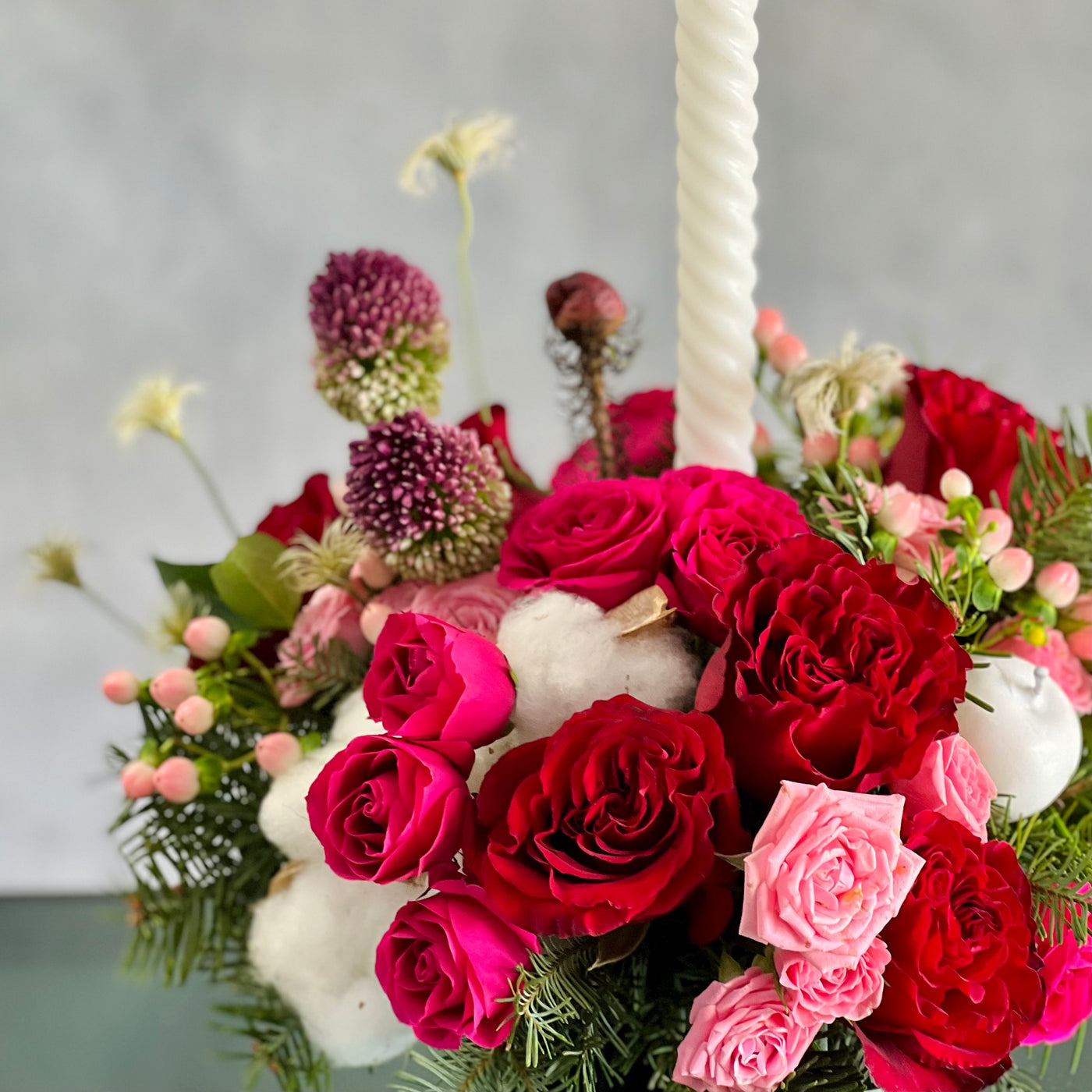 Festive Christmas centerpiece with red and pink roses, seasonal greens, berries, and glowing tapers, approx. 14 inches tall, for same-day delivery.