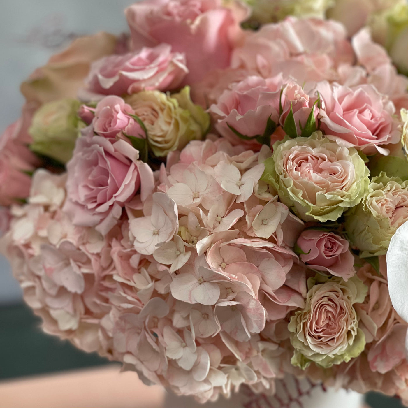 Dancing on the Clouds arrangement featuring soft pink hydrangeas, roses, spray roses, and white orchids in a chic white ceramic vase, perfect for all occasions.