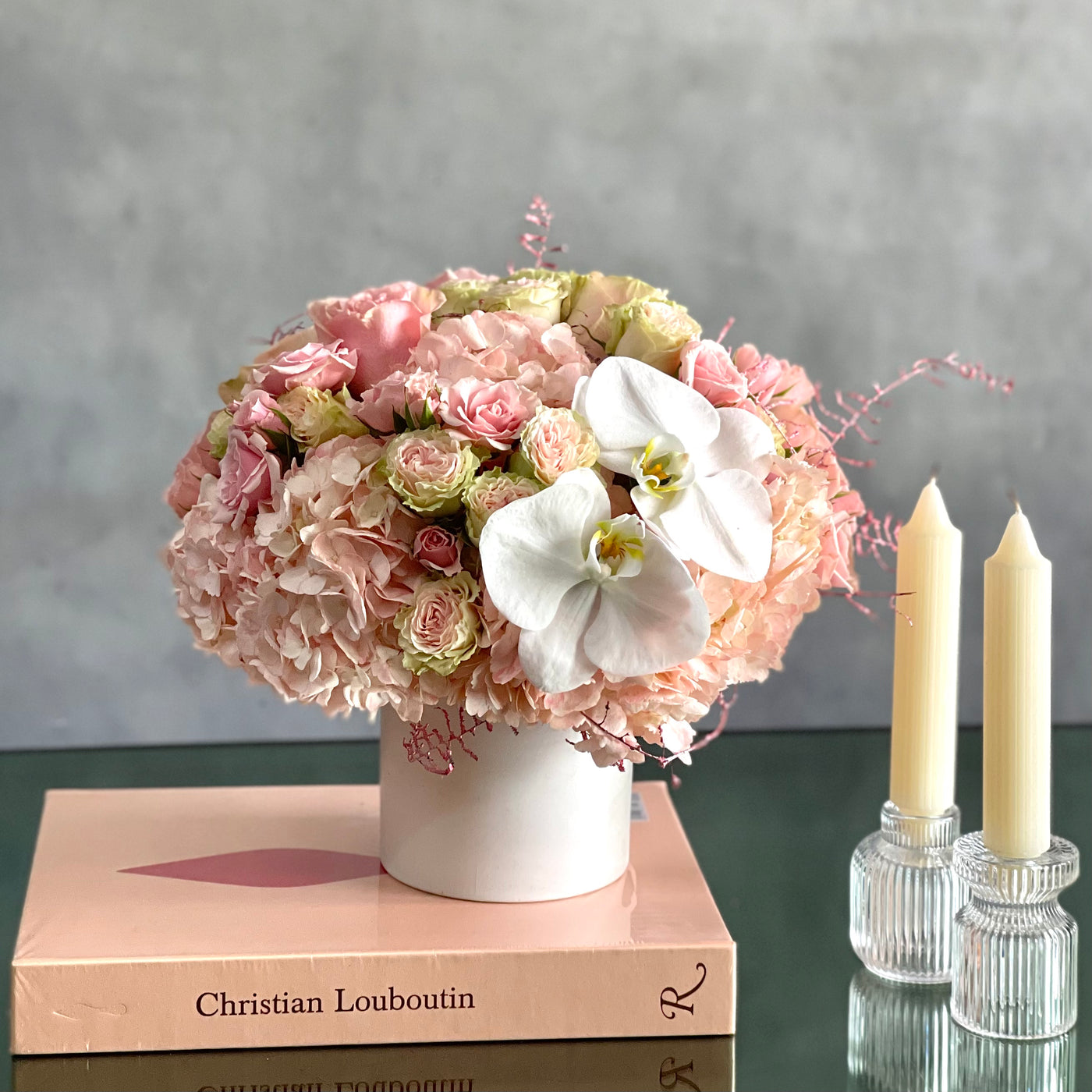 Dancing on the Clouds arrangement featuring soft pink hydrangeas, roses, spray roses, and white orchids in a chic white ceramic vase, perfect for all occasions.