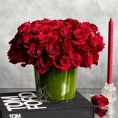 Kiss from a Rose arrangement with up to 75 fresh roses in a minimalist 7-inch glass vase lined with leaves, measuring 14 inches tall and 15 inches wide.