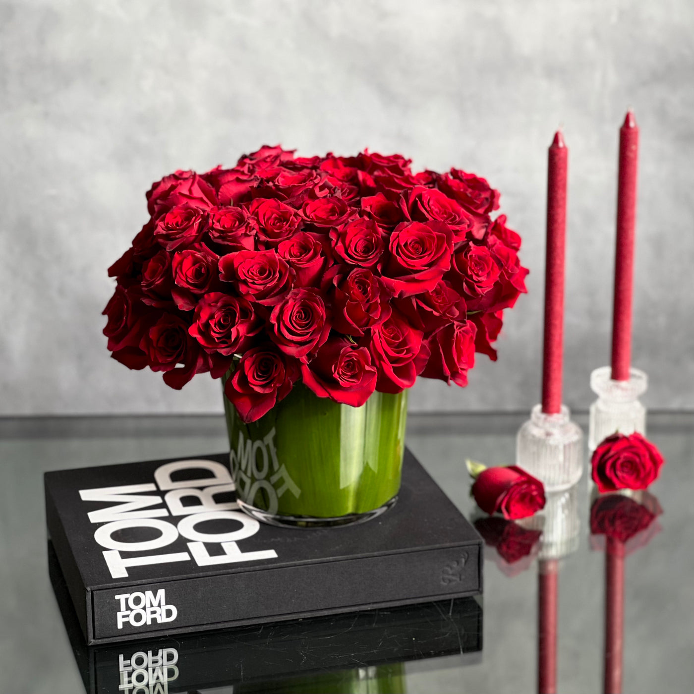 Kiss from a Rose arrangement with up to 75 fresh roses in a minimalist 7-inch glass vase lined with leaves, measuring 14 inches tall and 15 inches wide.