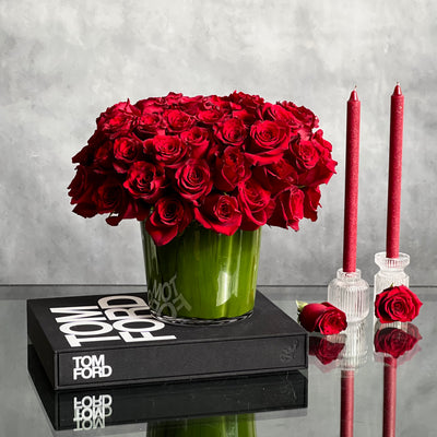 Kiss from a Rose arrangement with up to 75 fresh roses in a minimalist 7-inch glass vase lined with leaves, measuring 14 inches tall and 15 inches wide.