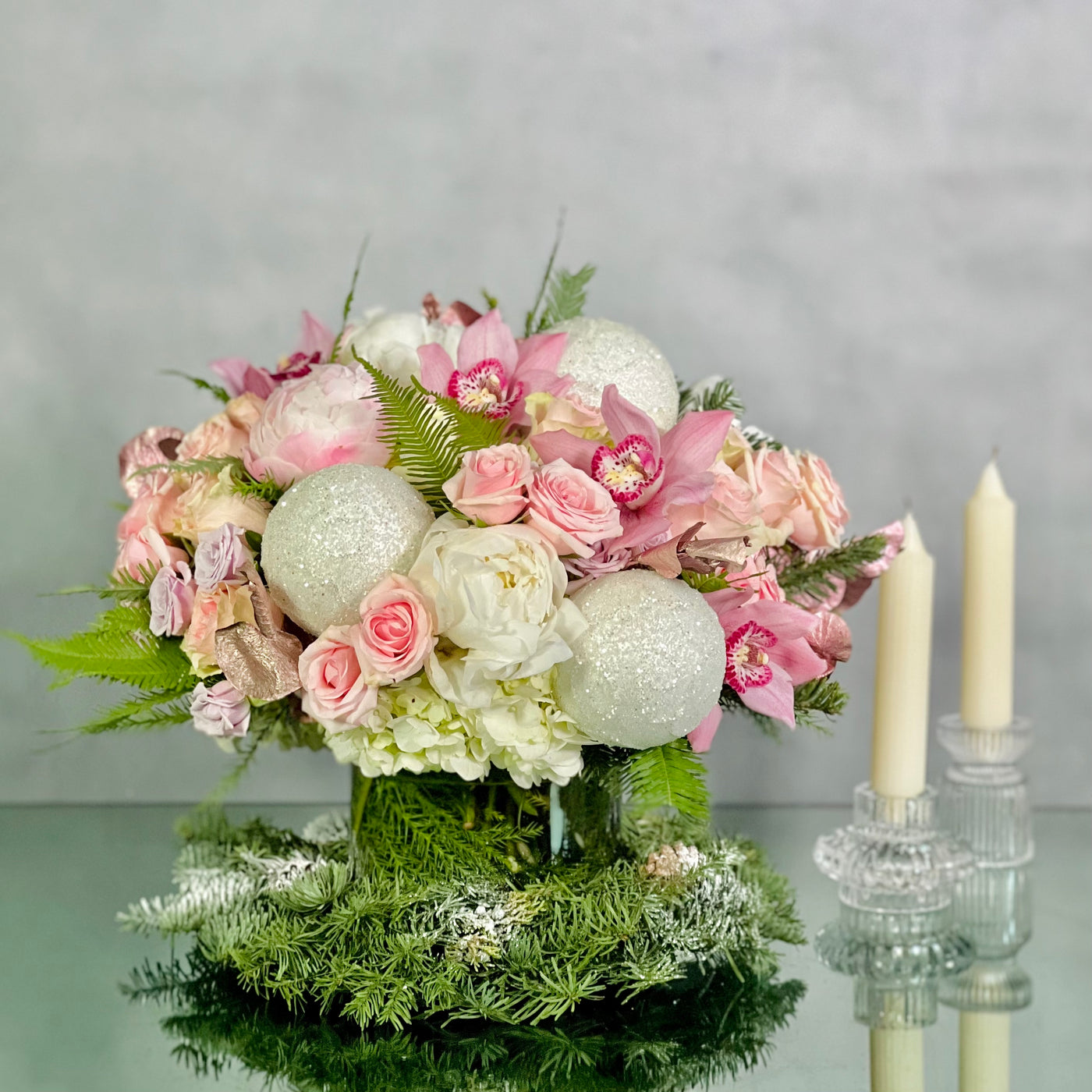 Pink Holiday arrangement featuring pink orchids, peonies, roses, and winter greens in a glass vase, available for same-day delivery by Beverly Hills Florist.