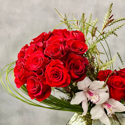 Elegant arrangement of 50 red roses with white Cymbidium orchids and seasonal greens in a geometric vase – Rosalicious by Beverly Hills Florist.