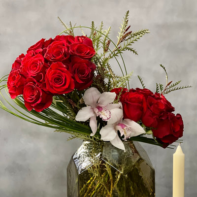 Elegant arrangement of 50 red roses with white Cymbidium orchids and seasonal greens in a geometric vase – Rosalicious by Beverly Hills Florist.