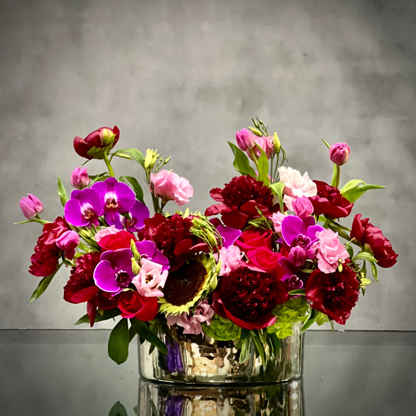 Luxurious Burgundy peony, lavender tulip, and purple orchid arrangement in a silver container with pale green accents, same-day delivery Beverly Hills.
