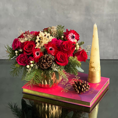 Yuletide Spirit holiday floral arrangement with red roses, spray roses, natural accents, and a gold ornament in a brushed gold cylinder vase.