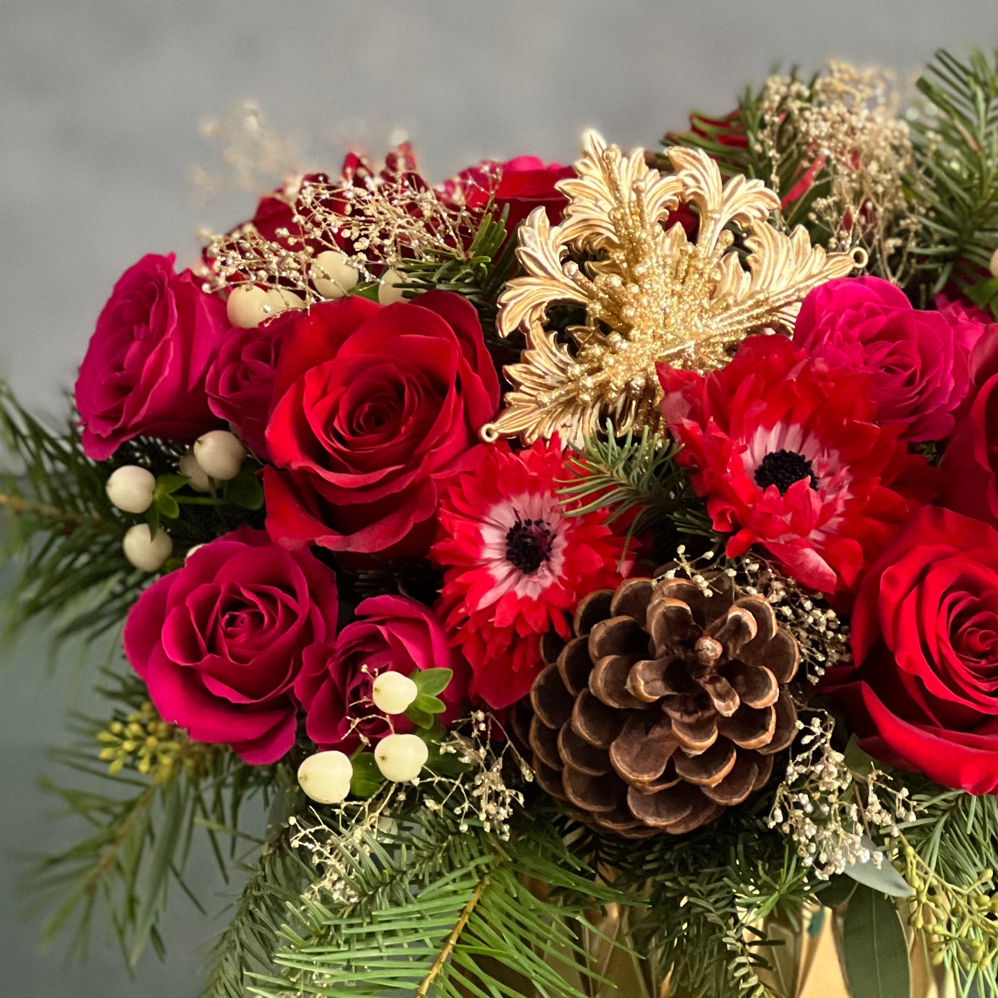 Yuletide Spirit holiday floral arrangement with red roses, spray roses, natural accents, and a gold ornament in a brushed gold cylinder vase.