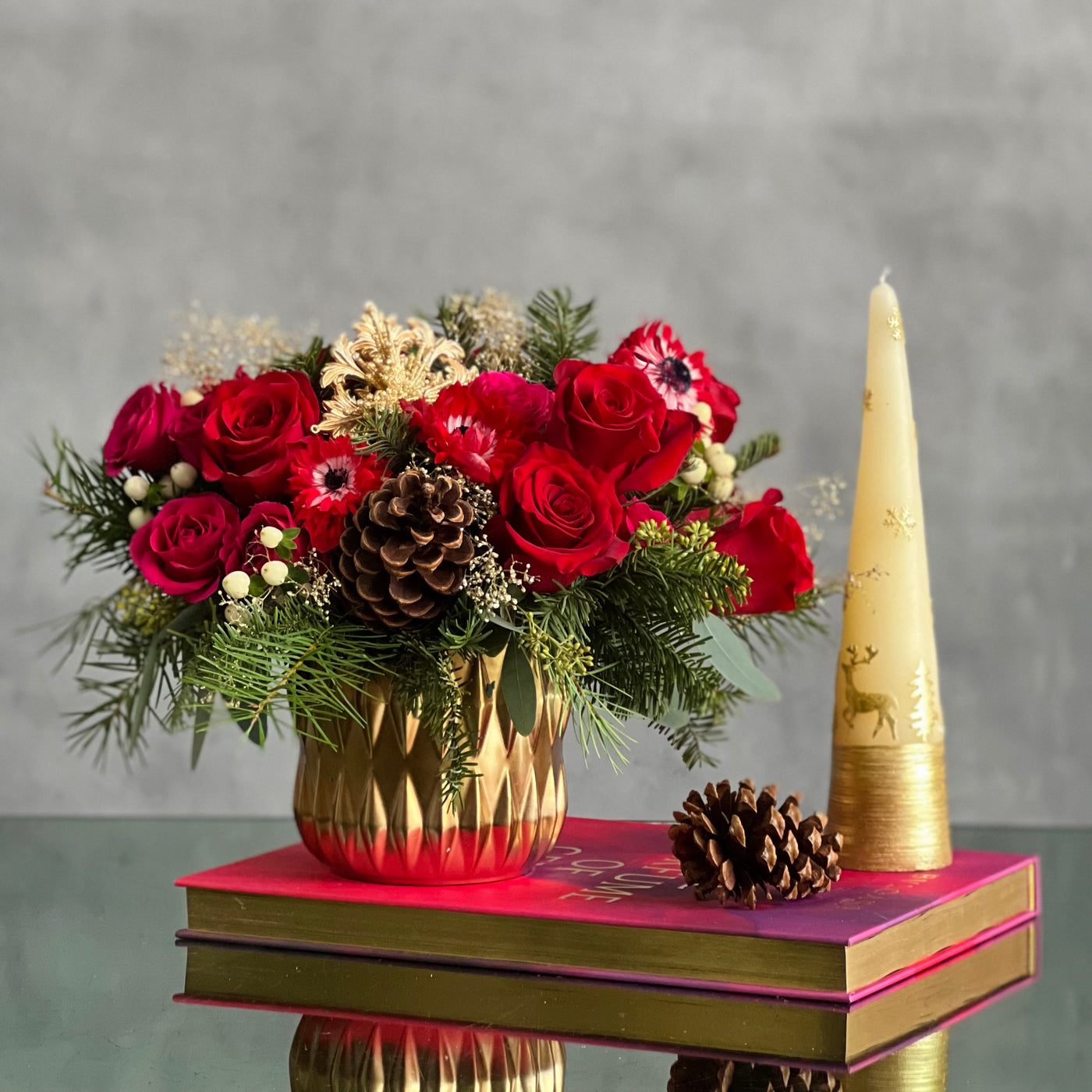 Yuletide Spirit holiday floral arrangement with red roses, spray roses, natural accents, and a gold ornament in a brushed gold cylinder vase.